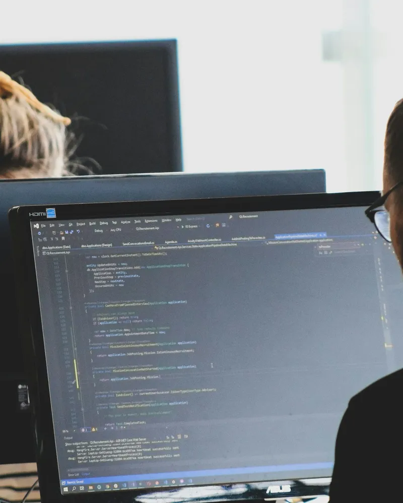 Two developers writing code at their monitors in a bright office